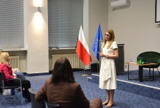 Na środku auli stoi Pani i przemawia przed uczestnikami