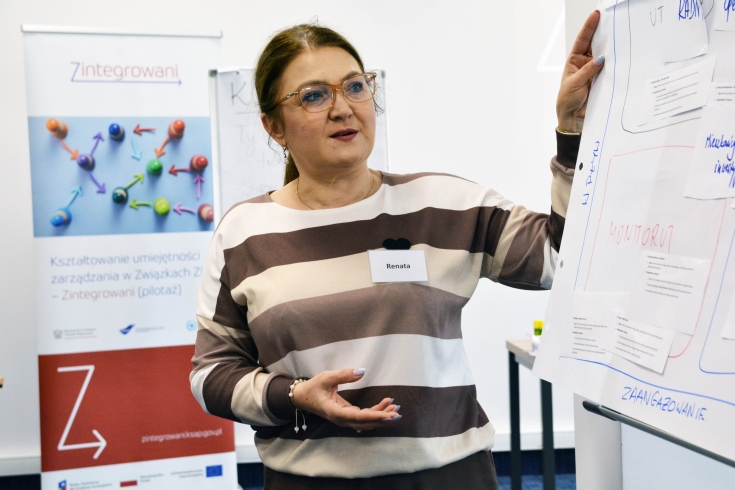 uczestniczka stoi przy flipczarcie, w tle baner projektu